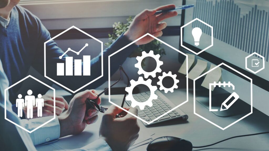 Two people discuss business analytics at a desk with overlaid icons representing growth, teamwork, innovation, and strategy, using information technology to improve business processes shown on a computer displaying a bar chart.