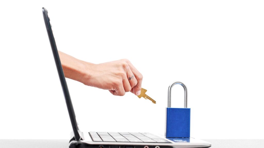 A hand holds a key toward a blue padlock on a laptop keyboard, symbolizing how to protect your computer and ensure strong computer security against hackers.