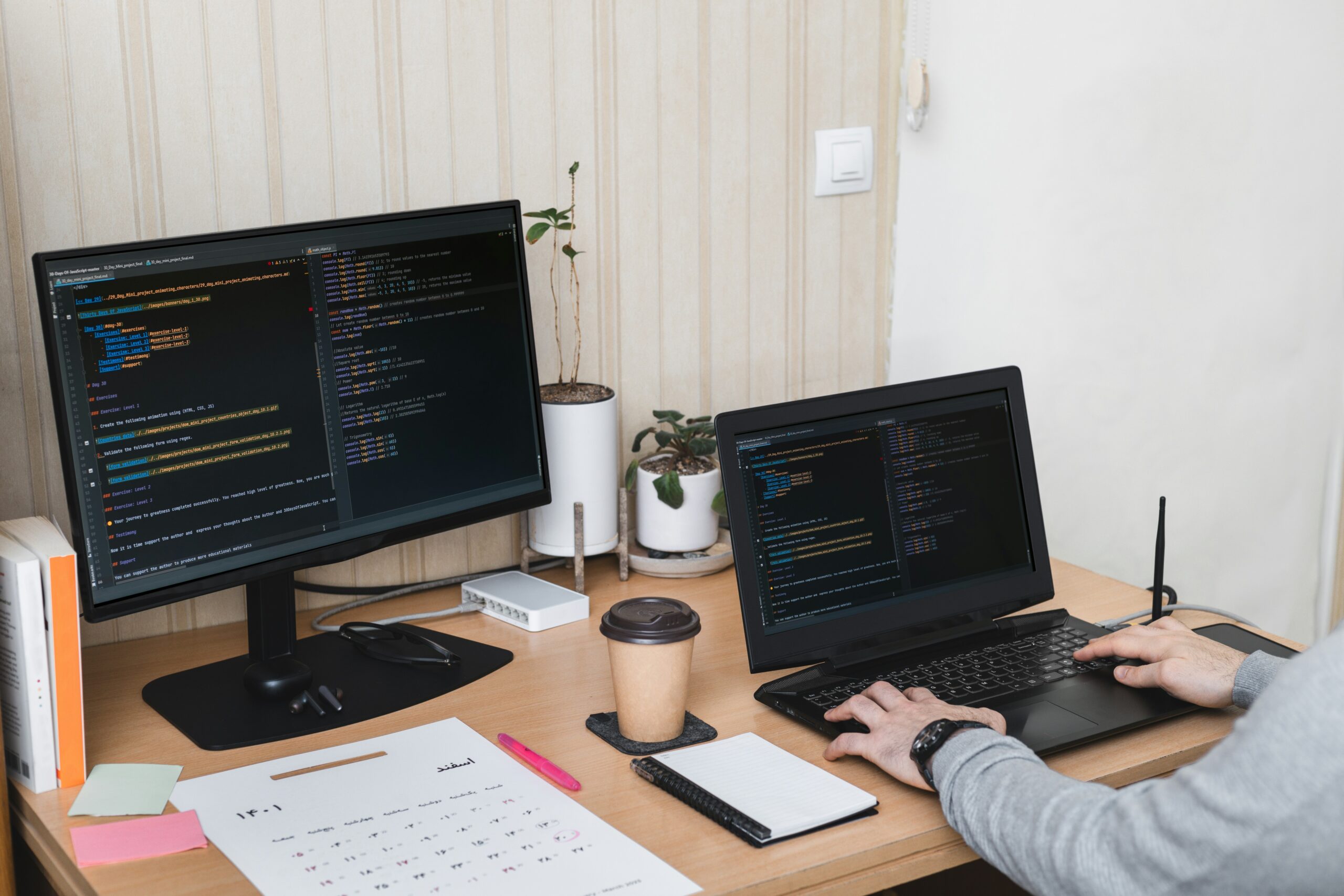 A man sitting at a desk with two laptops and a notebook, exploring cyber security tips like how to secure network.