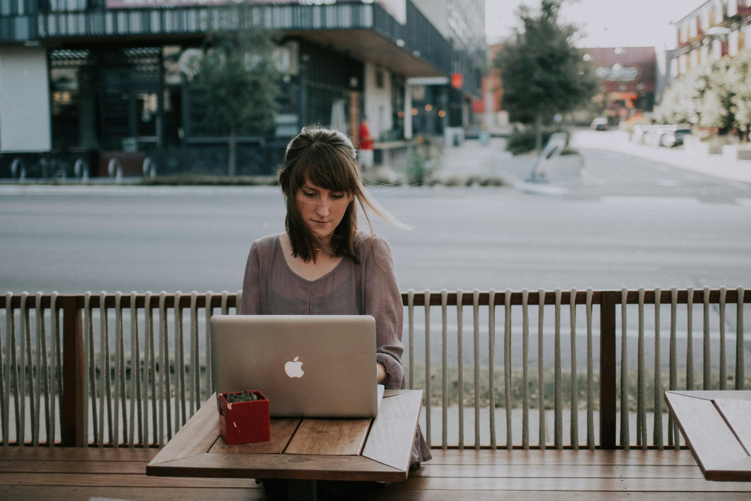 A woman sits at an outdoor table working on a laptop, pondering, why do I need Office 365.
