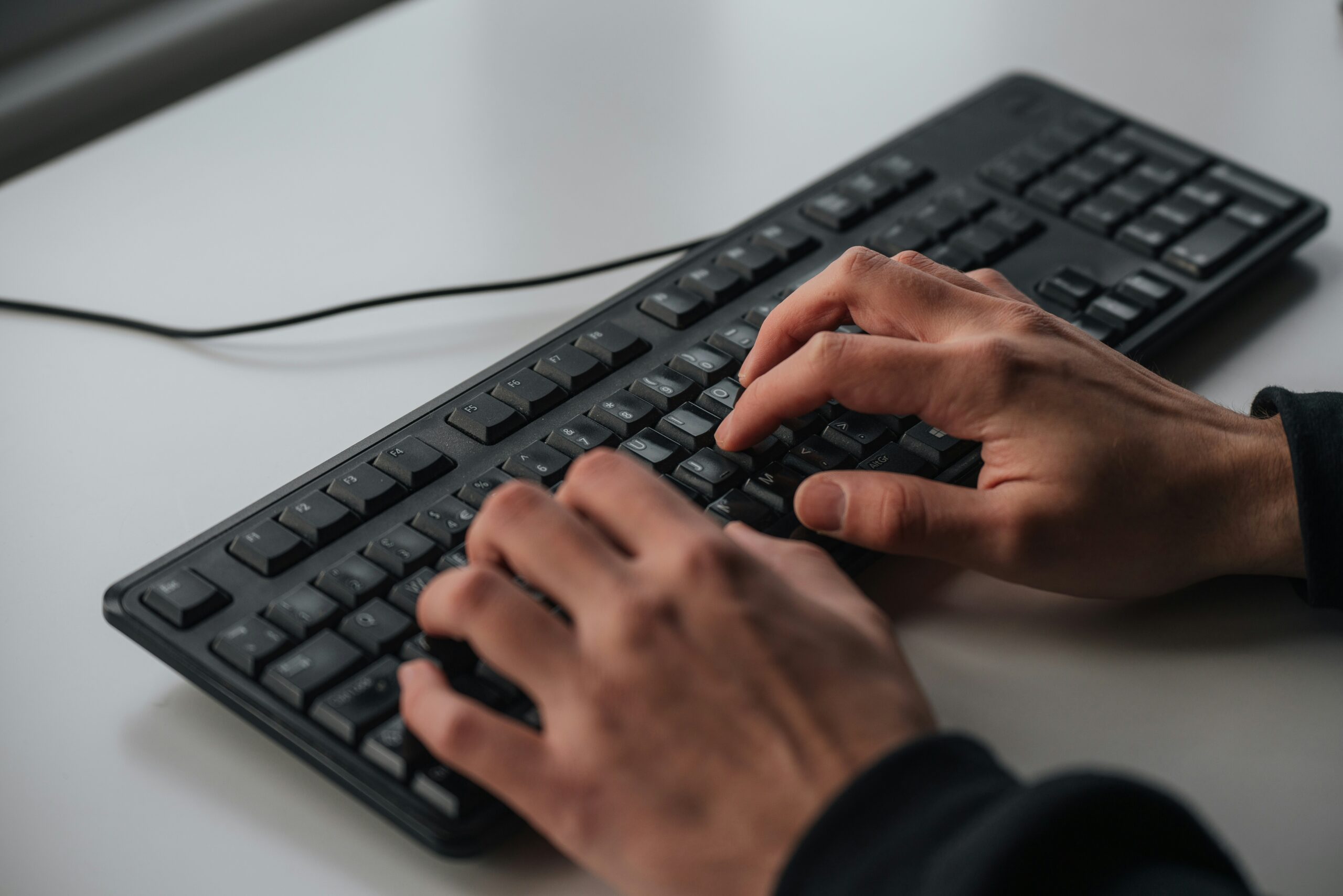 Hands typing on a black computer keyboard to research, why do I need Office 365.
