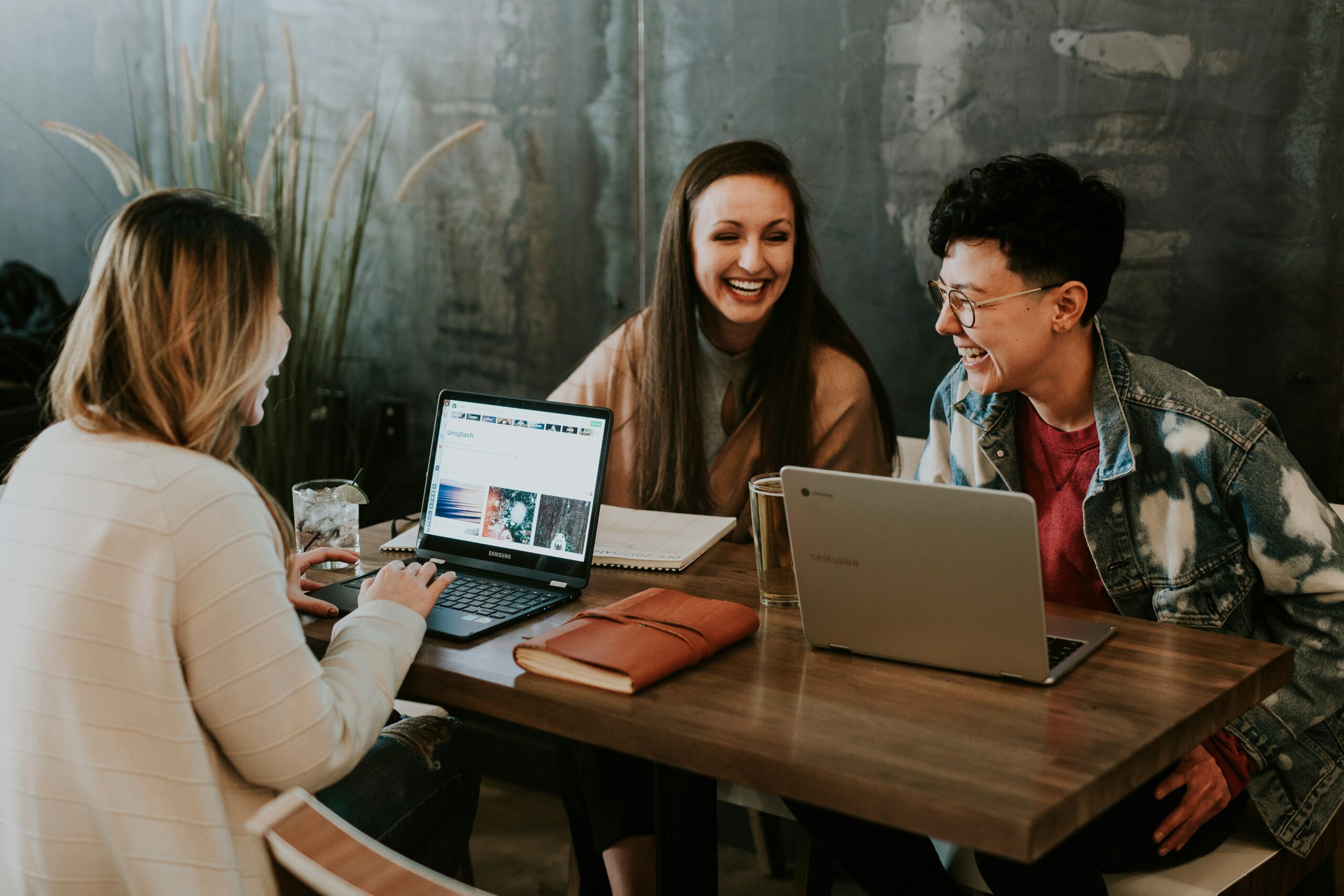 Three people are sitting at a wooden table, using laptops and debating the difference between Microsoft Office and Office 365.