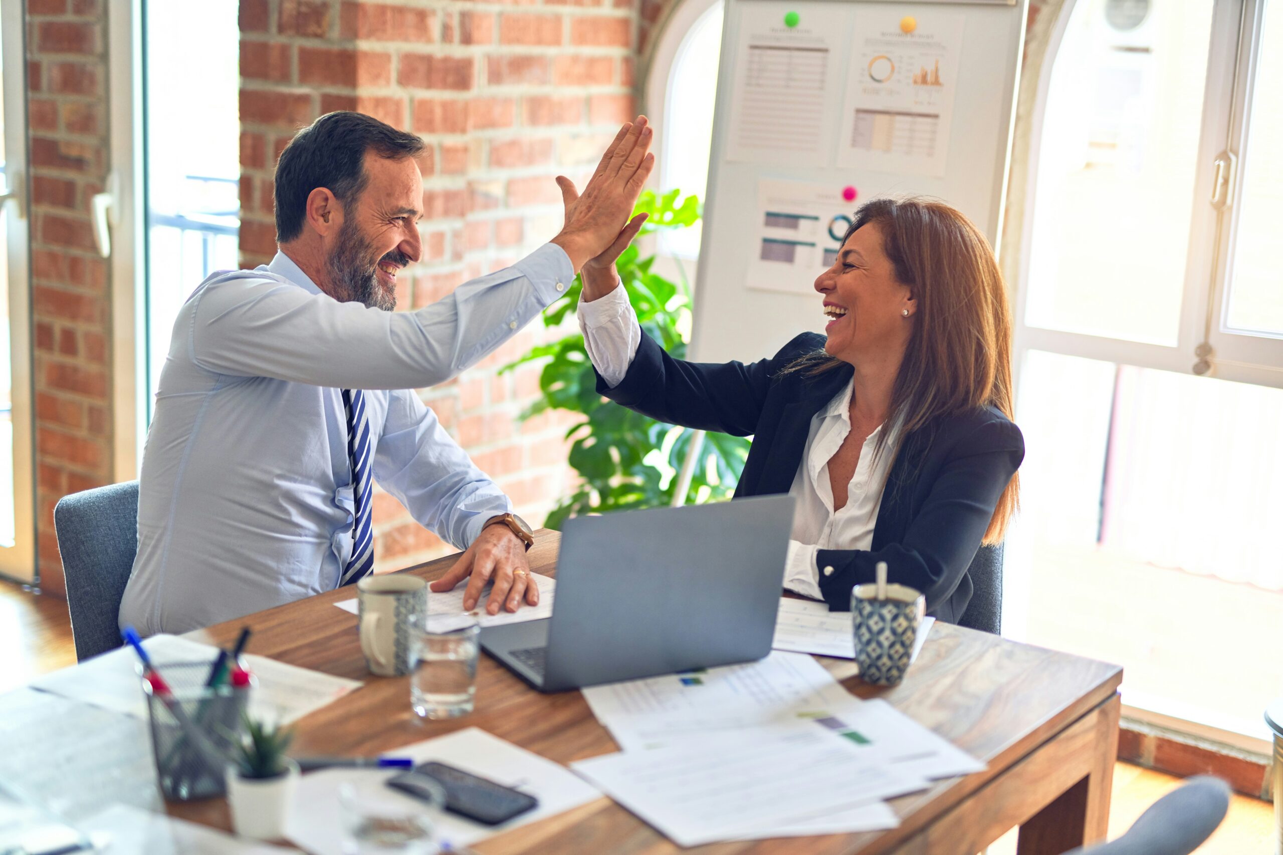 Two business people giving each other high fives in an office after sharing cyber security tips.